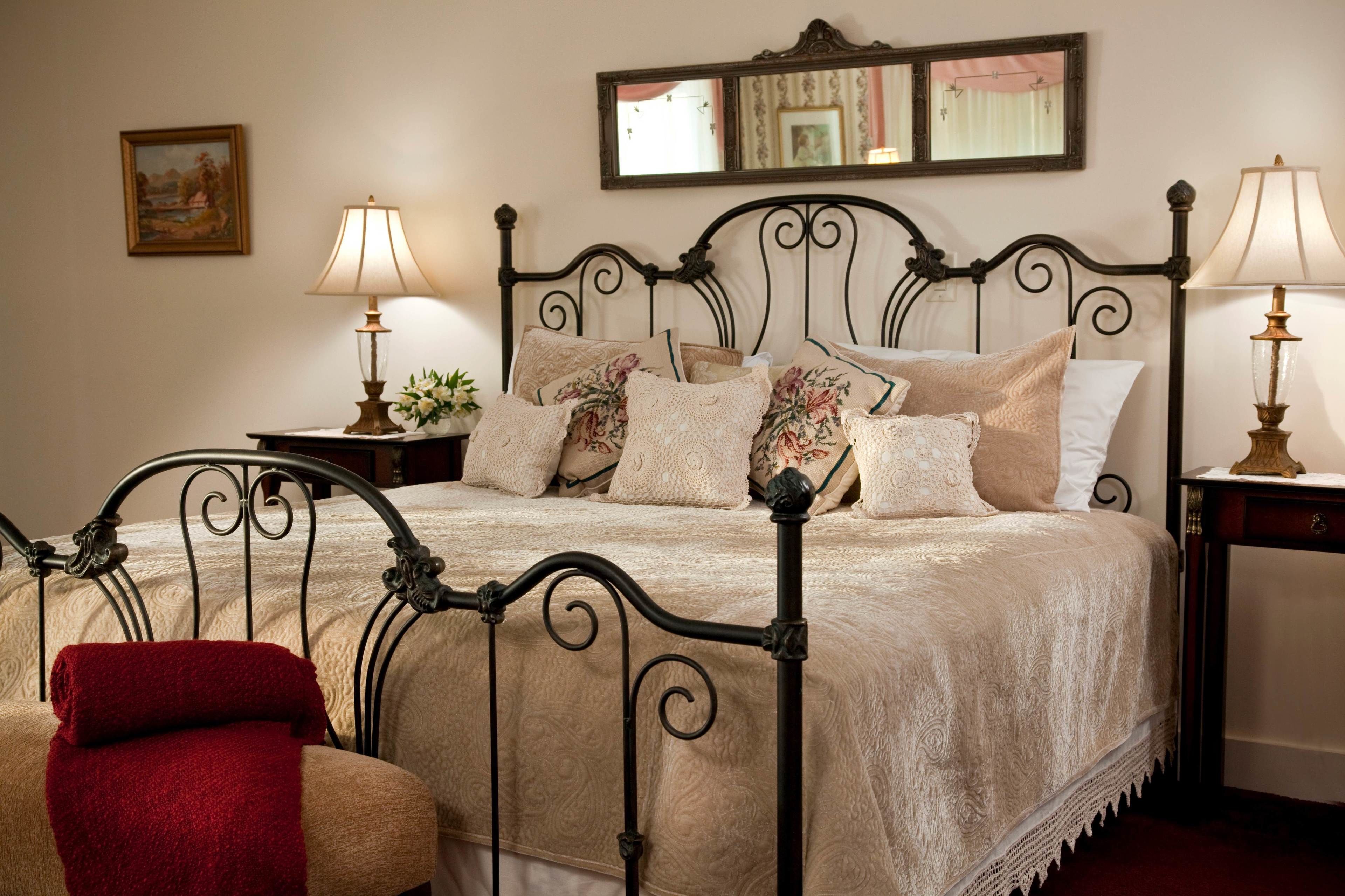A neatly made bed with a floral-patterned bedspread, two bedside tables with lamps, and a red throw on the chair.