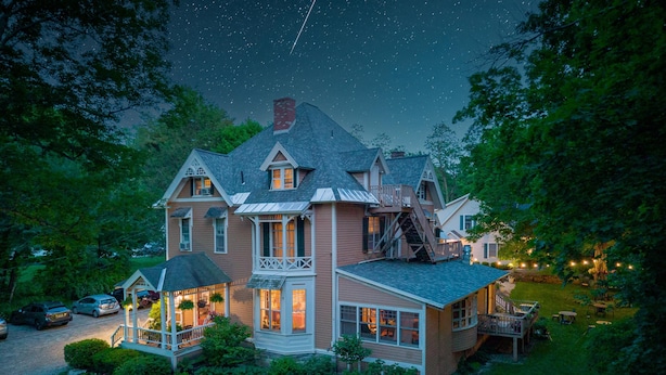 Een groot, twee verdiepingen tellend huis met een brede veranda en een overdekte voortuin.