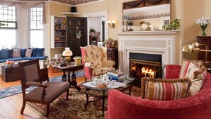 Een gezellige woonkamer met een open haard, een blauwe bank, een rode fauteuil en een bijzettafeltje met boeken en een theepot.