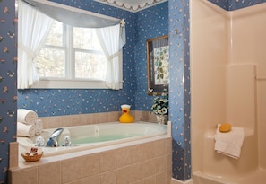 A bathroom with a bathtub, a window with curtains, a mirror, and a shower area.
