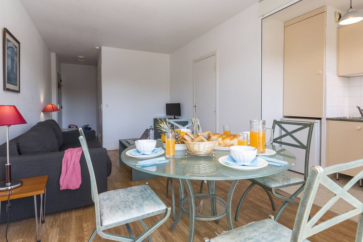 Ein modernes Wohnzimmer mit einem Esstisch aus Glas, gedeckt für das Frühstück, einer Couch und einem Fernseher im Hintergrund.