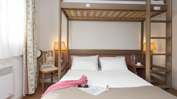 A hotel room with a bunk bed, a chair, a bedside table with a lamp, and a window with curtains. - Résidence Green Panorama (Varaville)
