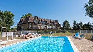 A swimming pool with lounge chairs and a large building in the background. - Résidence Green Panorama (Varaville)