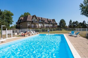 A swimming pool with lounge chairs and a large building in the background. - Résidence Green Panorama (Varaville)