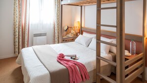 Une chambre d’hôtel avec un lit superposé, une lampe de chevet, une valise et une fenêtre avec des rideaux.