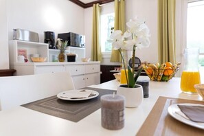 A breakfast setting with a table set for two, a fruit bowl, a vase with flowers, and a coffee maker. - Résidence Green Panorama (Varaville)
