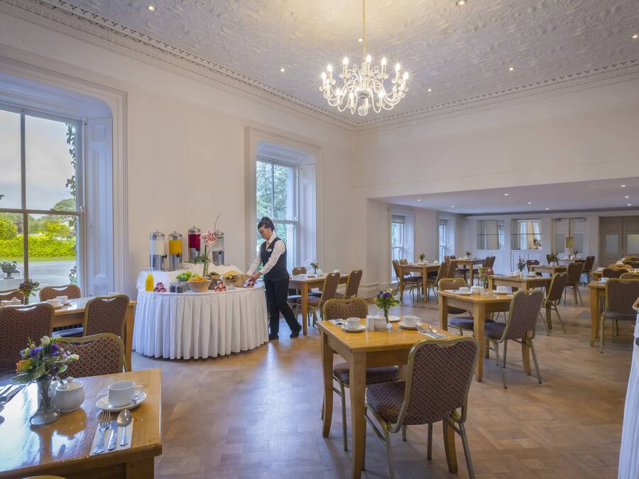 A spacious dining area with multiple tables, a chandelier, and a view of the outdoors.