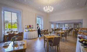A spacious dining area with multiple tables, a chandelier, and a view of the outdoors. - Boyne Valley Hotel - Bed & Breakfast Only (Drogheda)