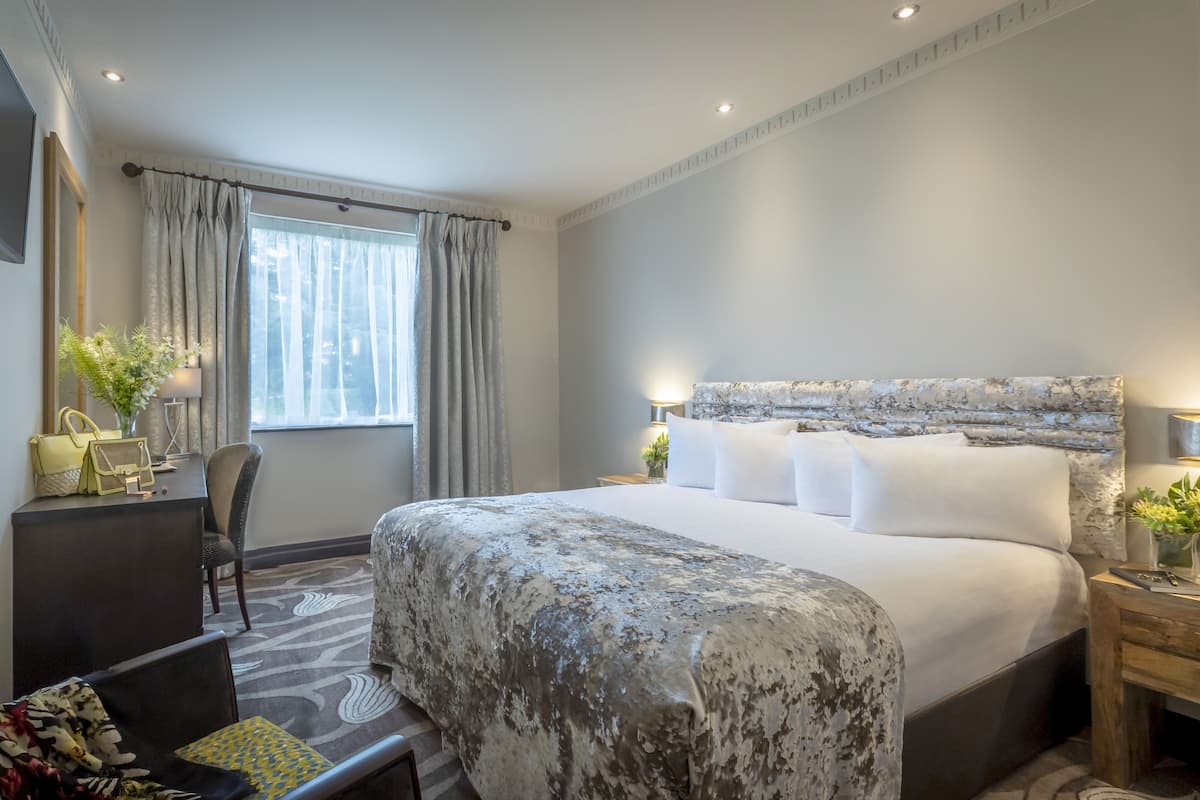 Habitación de hotel con una cama grande, un escritorio con silla, televisor montado en la pared y una ventana con cortinas.