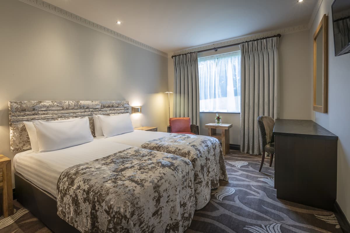 Una habitación de hotel con una cama grande, dos mesitas de noche, un escritorio, una silla y un televisor.