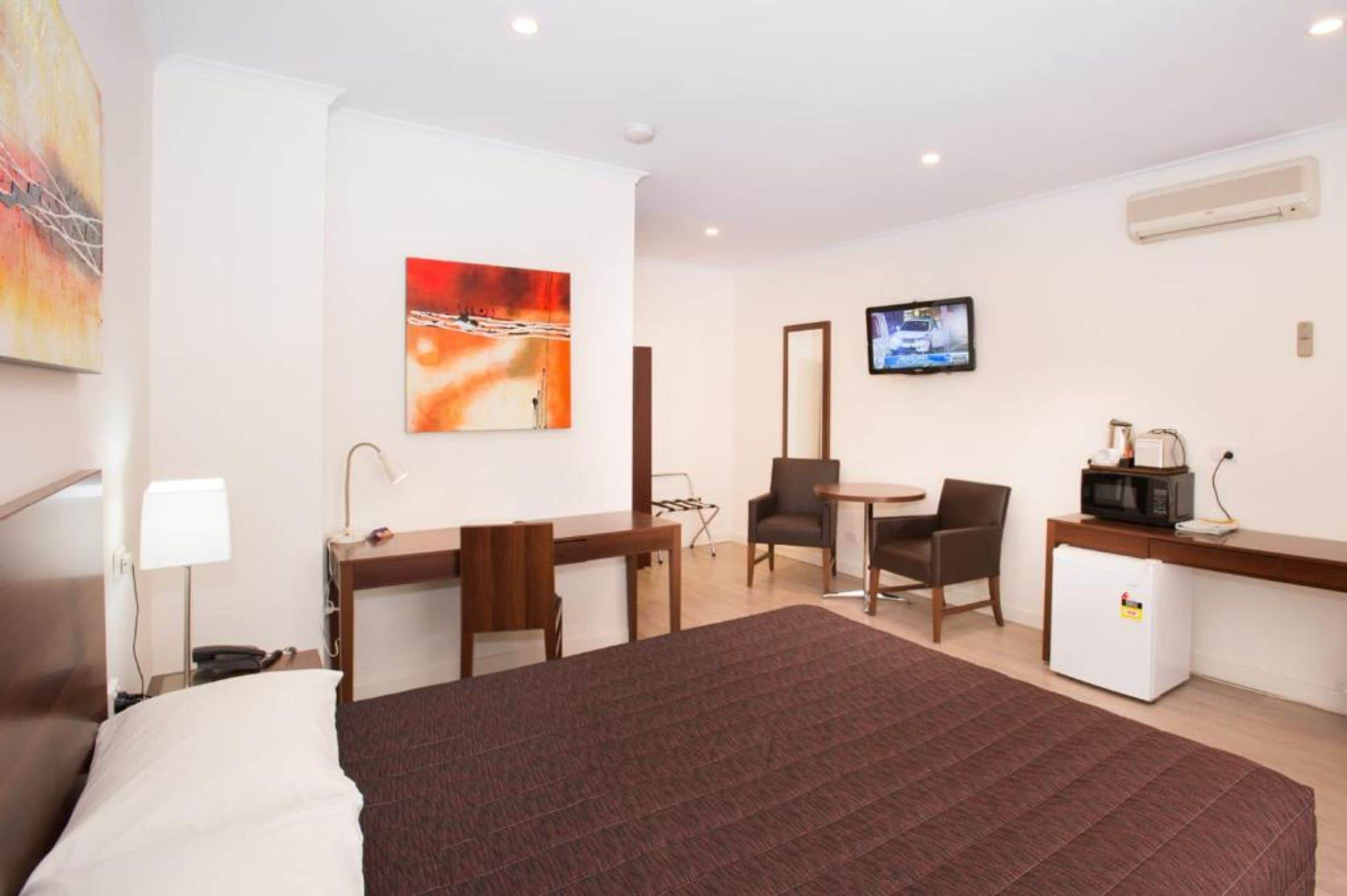 A hotel room with a bed, desk, chairs, a television, and a refrigerator.
