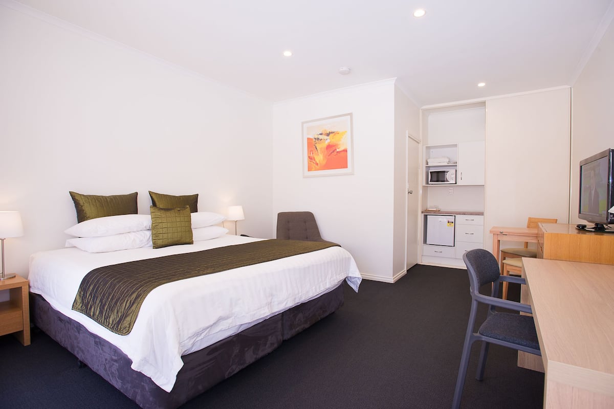 Quarto de hotel com cama, escrivaninha, cadeira, micro-ondas e televisão.