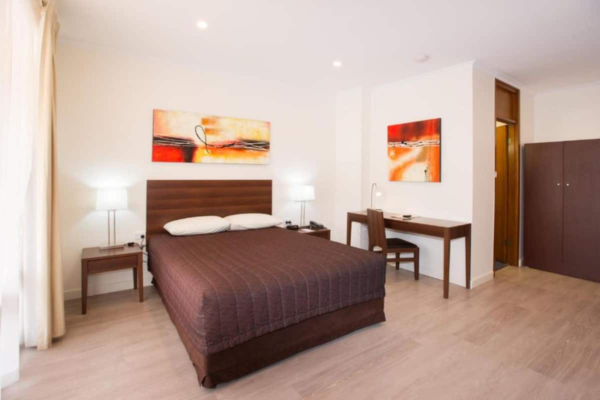 Quarto com cama, mesas de cabeceira, escrivaninha e cadeiras.