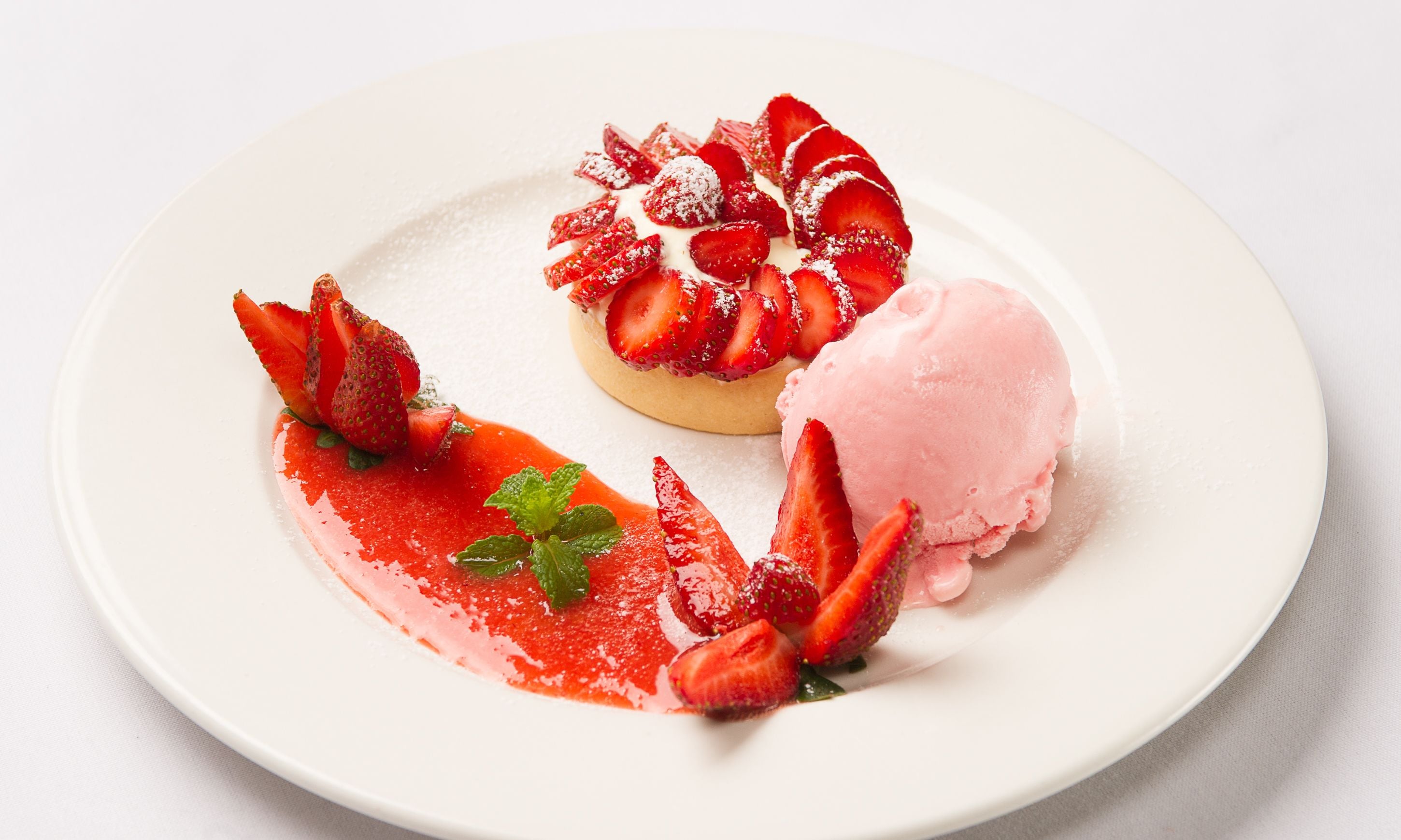 Un plato de postre con una tarta de fresa y una bola de helado rosa.