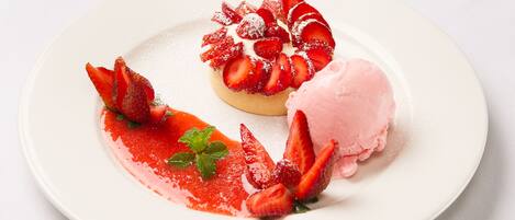 Un plato de postre con una tarta de fresa y una bola de helado rosa.