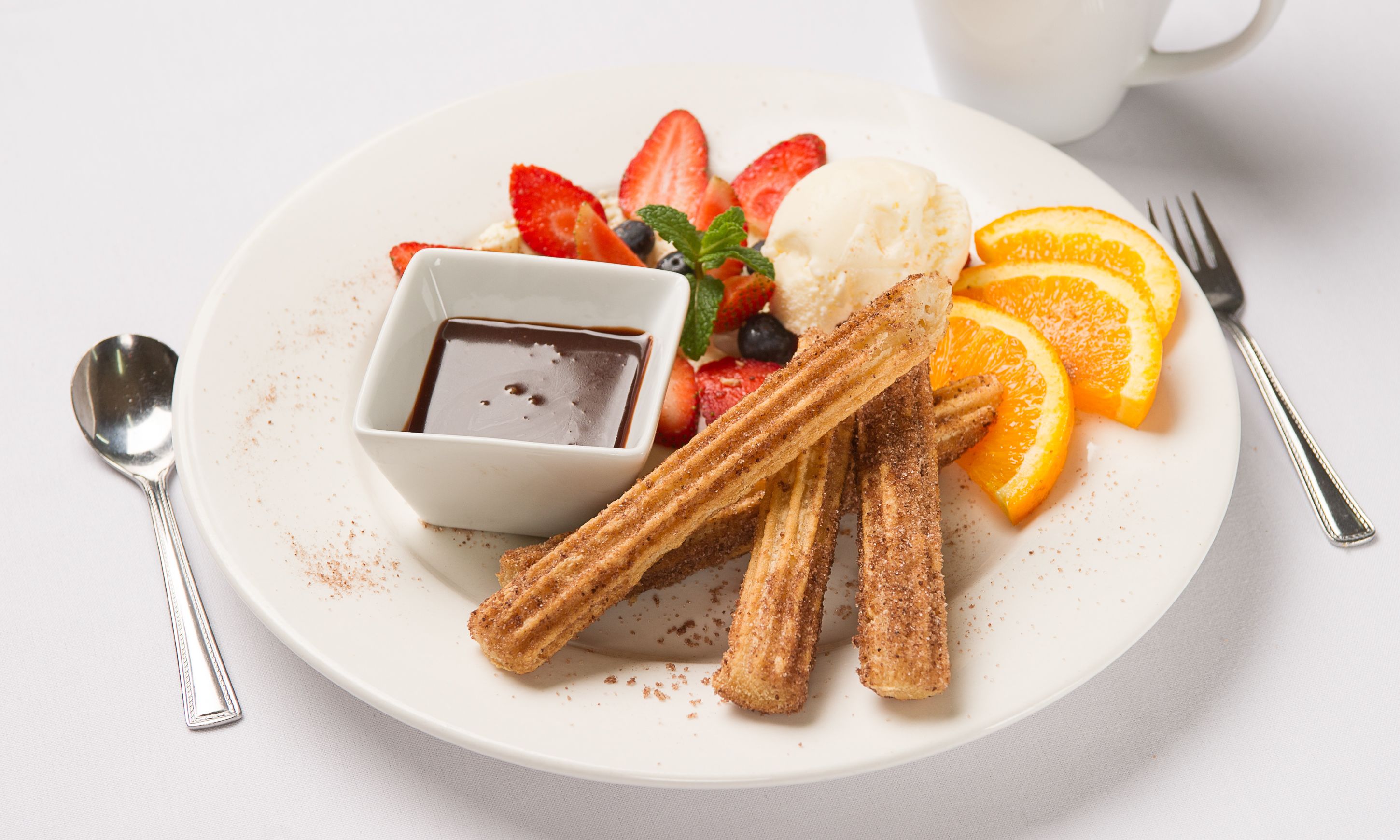 A plate with churros, ice cream, strawberries, blueberries, and orange slices.
