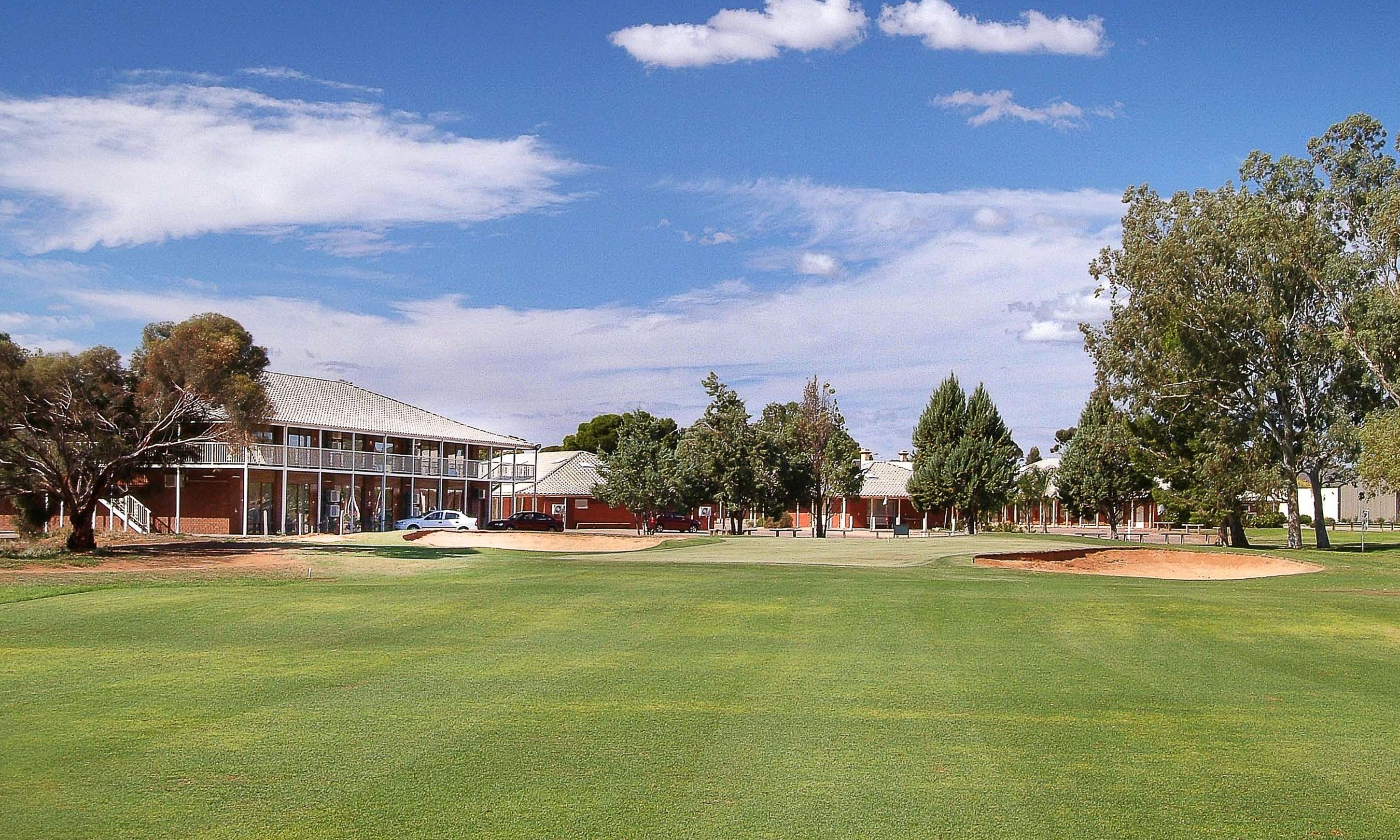 A golf course with a clubhouse, trees, and a clear sky.