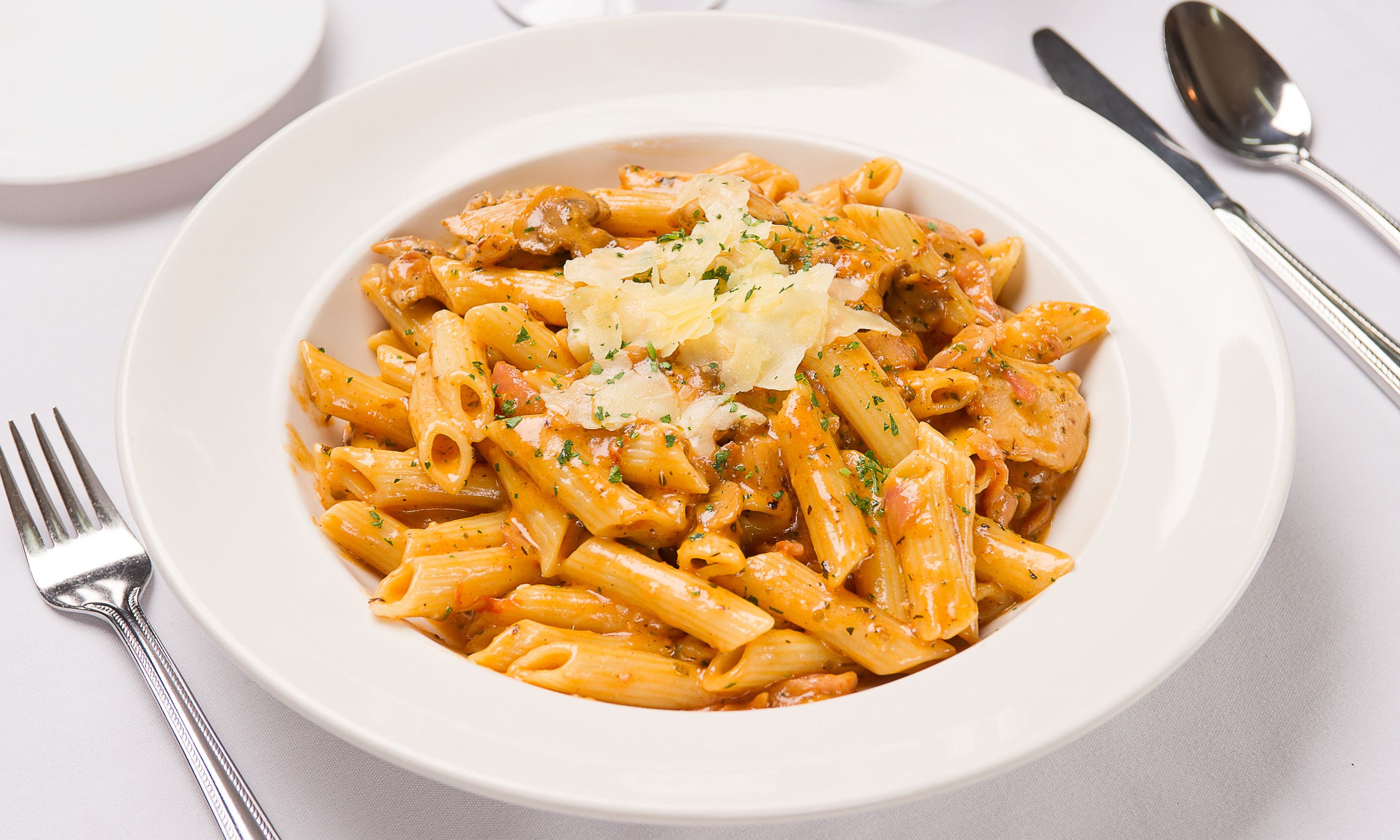 Lautasella on penne-pastaa, jonka päällä on tomaattipohjainen kastike, sekä tuoreita yrttejä ja raastettua juustoa.