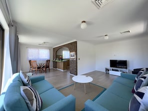Een moderne woonkamer met een bank, televisie en een eethoek met stoelen en een tafel.