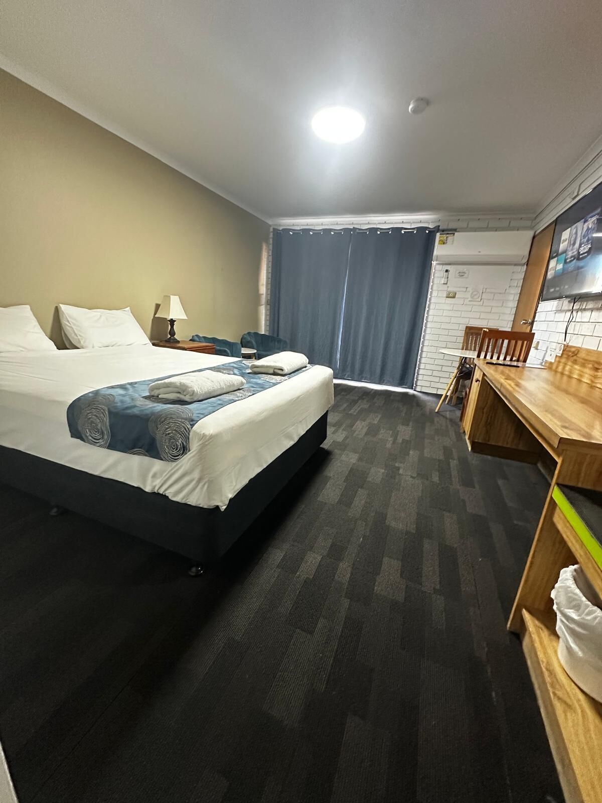 A hotel room with a bed, a desk, a chair, a TV, and a window with curtains.
