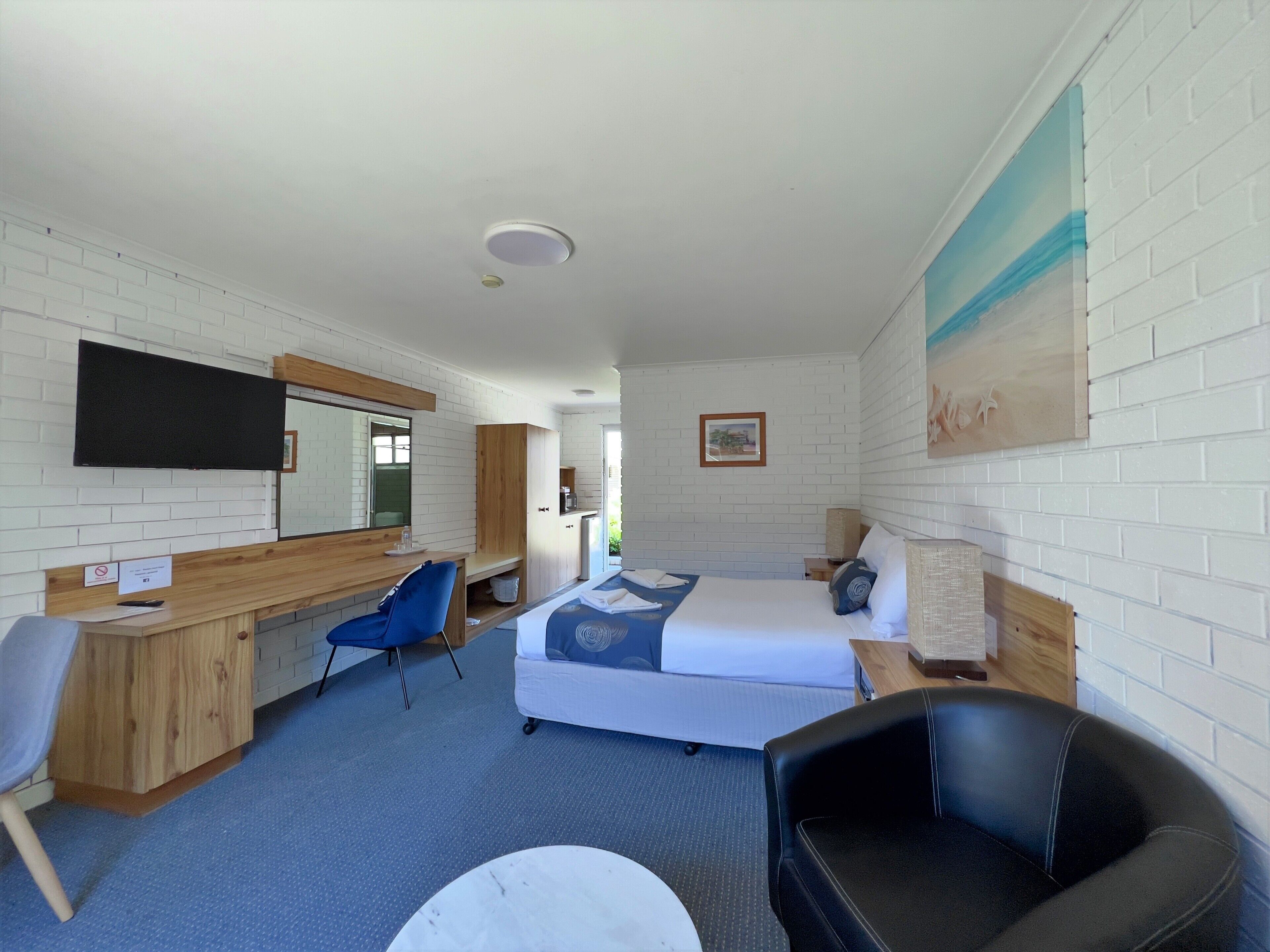 Una habitación de hotel con cama, escritorio, silla y televisor montado en la pared.