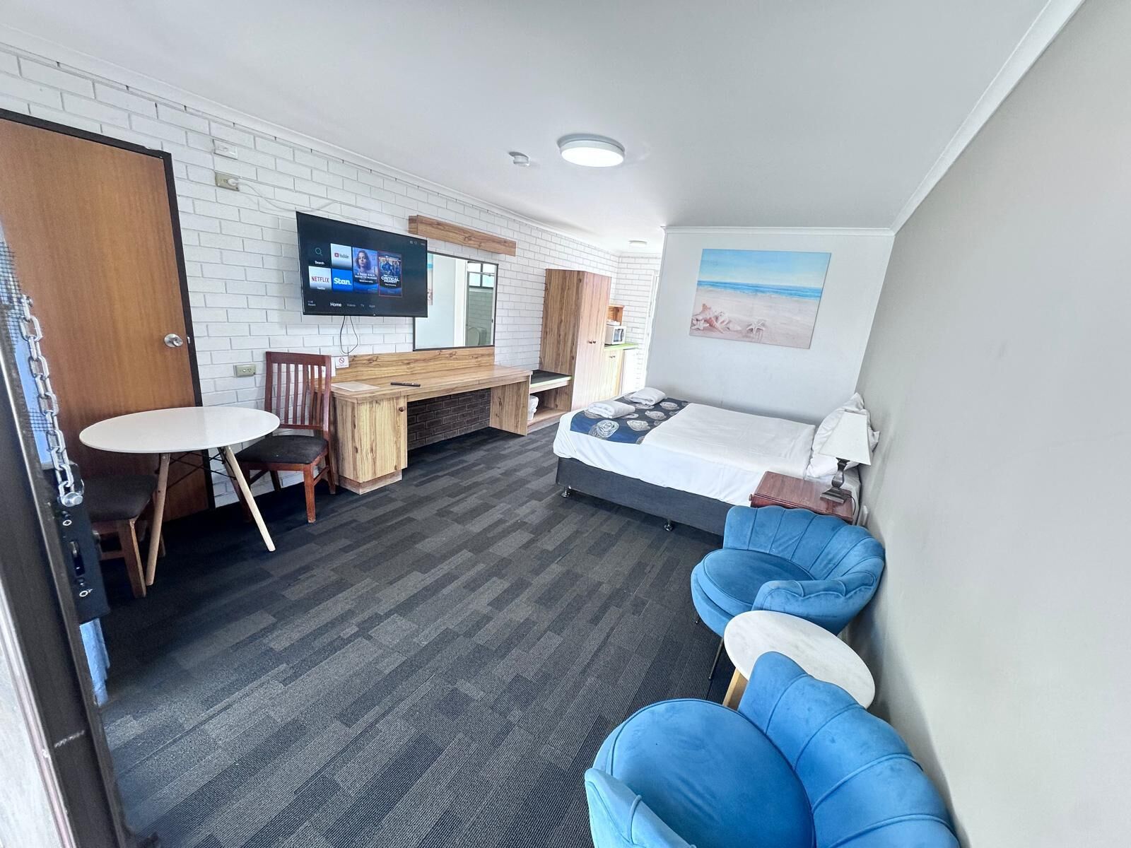 A modern hotel room with a bed, a desk, a TV, and a seating area.