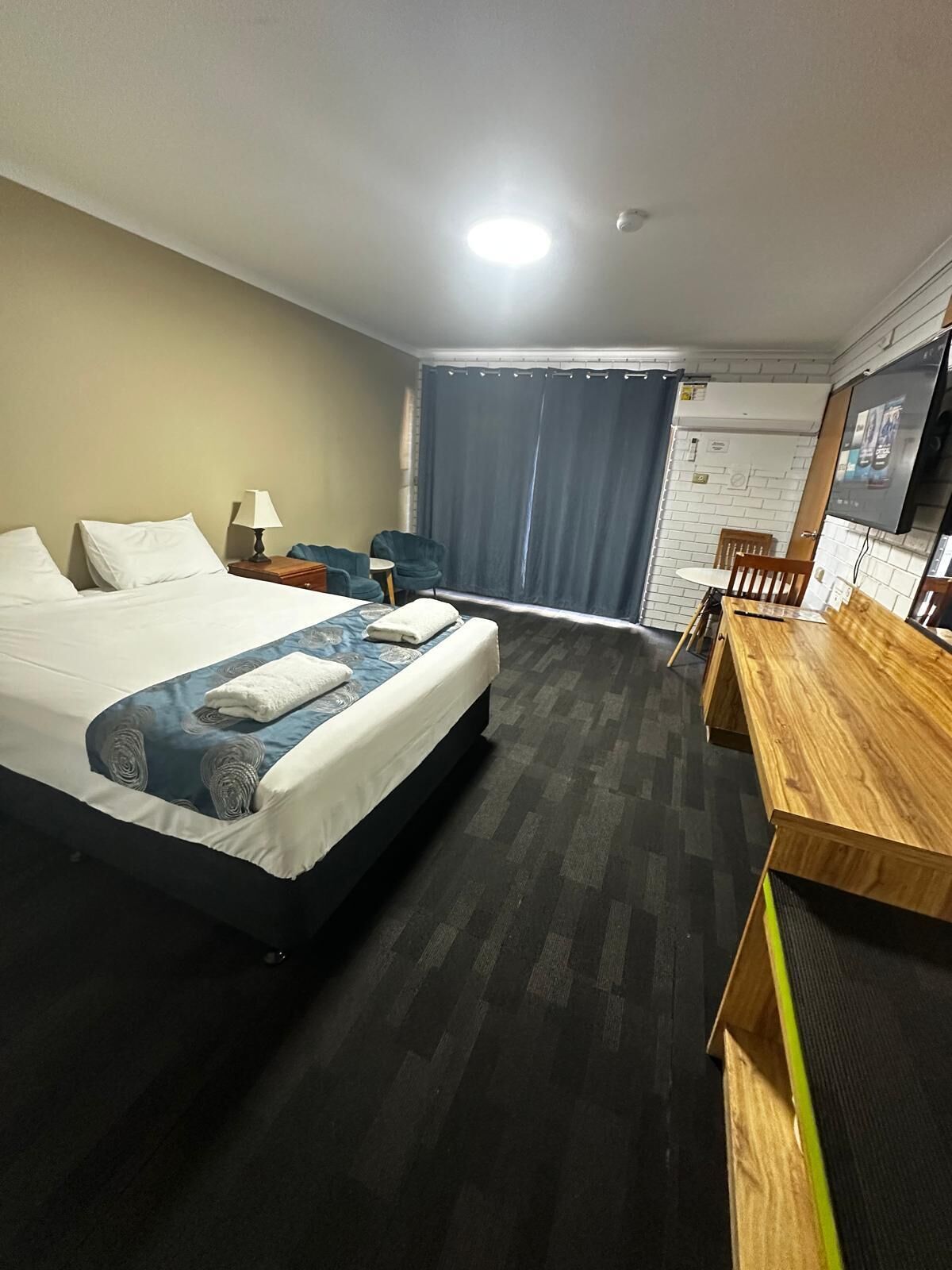 A hotel room with a large bed, a desk, a chair, a TV, and a window with curtains.