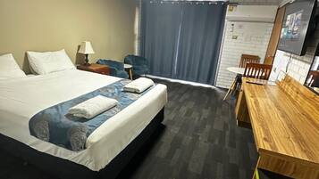 A hotel room with a large bed, a desk, a chair, a TV, and a window with curtains.