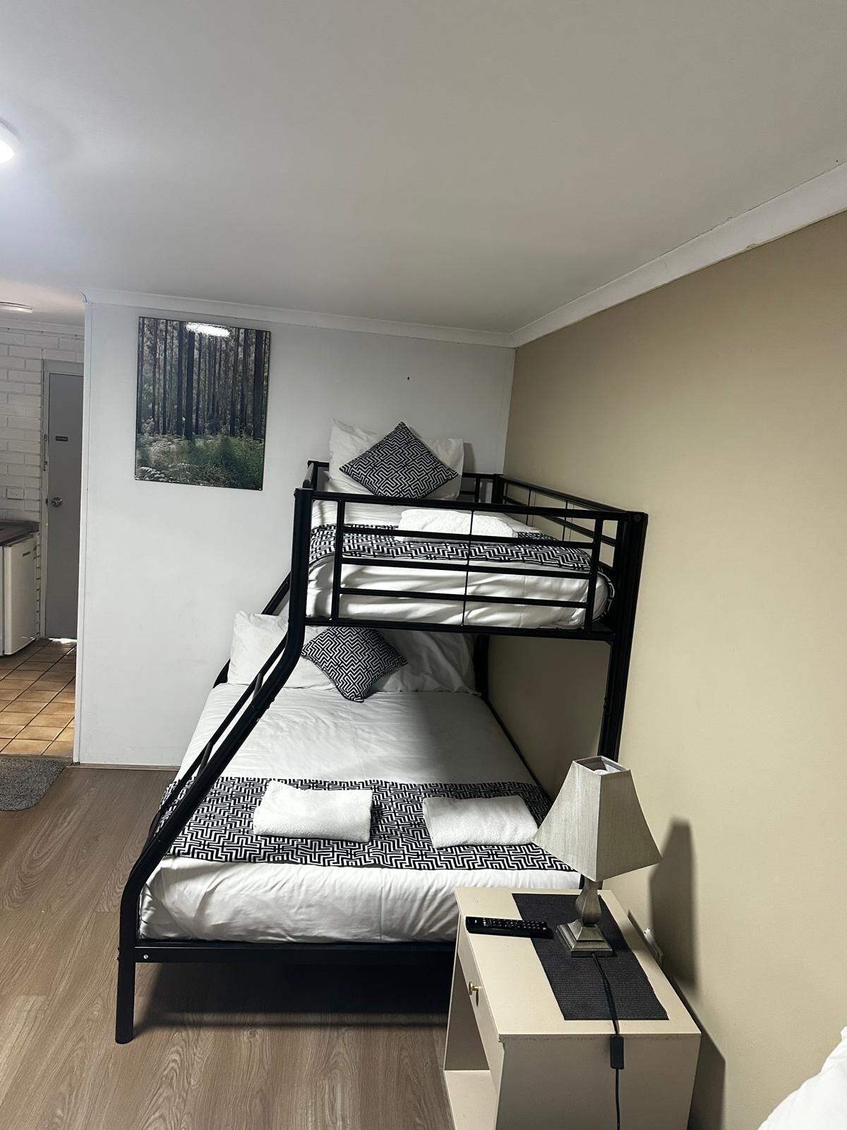 Uma cama beliche com roupa de cama estampada, uma escrivaninha com abajur e uma obra de arte na parede com tema de floresta.