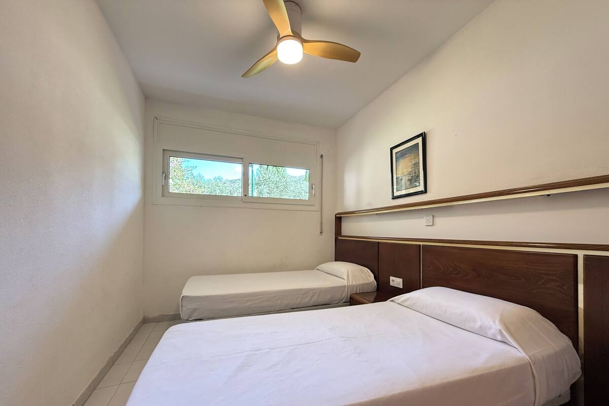 Un dormitorio con dos camas, un ventilador de techo, una ventana y un cuadro en la pared.