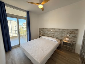 A bedroom with a bed, a ceiling fan, a view of the outside, and a wooden headboard.