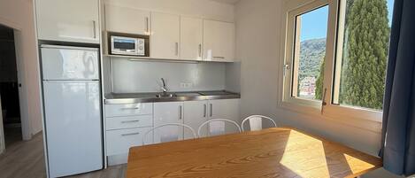 Une cuisine compacte avec des meubles blancs, un four à micro-ondes, un évier et un coin repas comprenant une table et des chaises en bois.