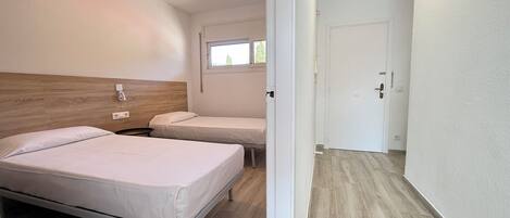 Habitación de hotel con dos camas, un ventilador de techo, una ventana y una puerta.
