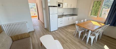 A modern kitchen with white cabinets, a dining area with a wooden table and white chairs, and a view of greenery outside.