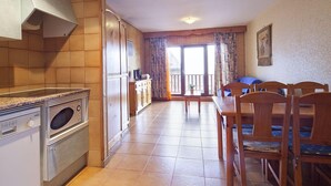 A kitchen with a microwave, oven, and cabinets, leading to a dining area with a table and chairs. - Kione Deusol (Soldeu)