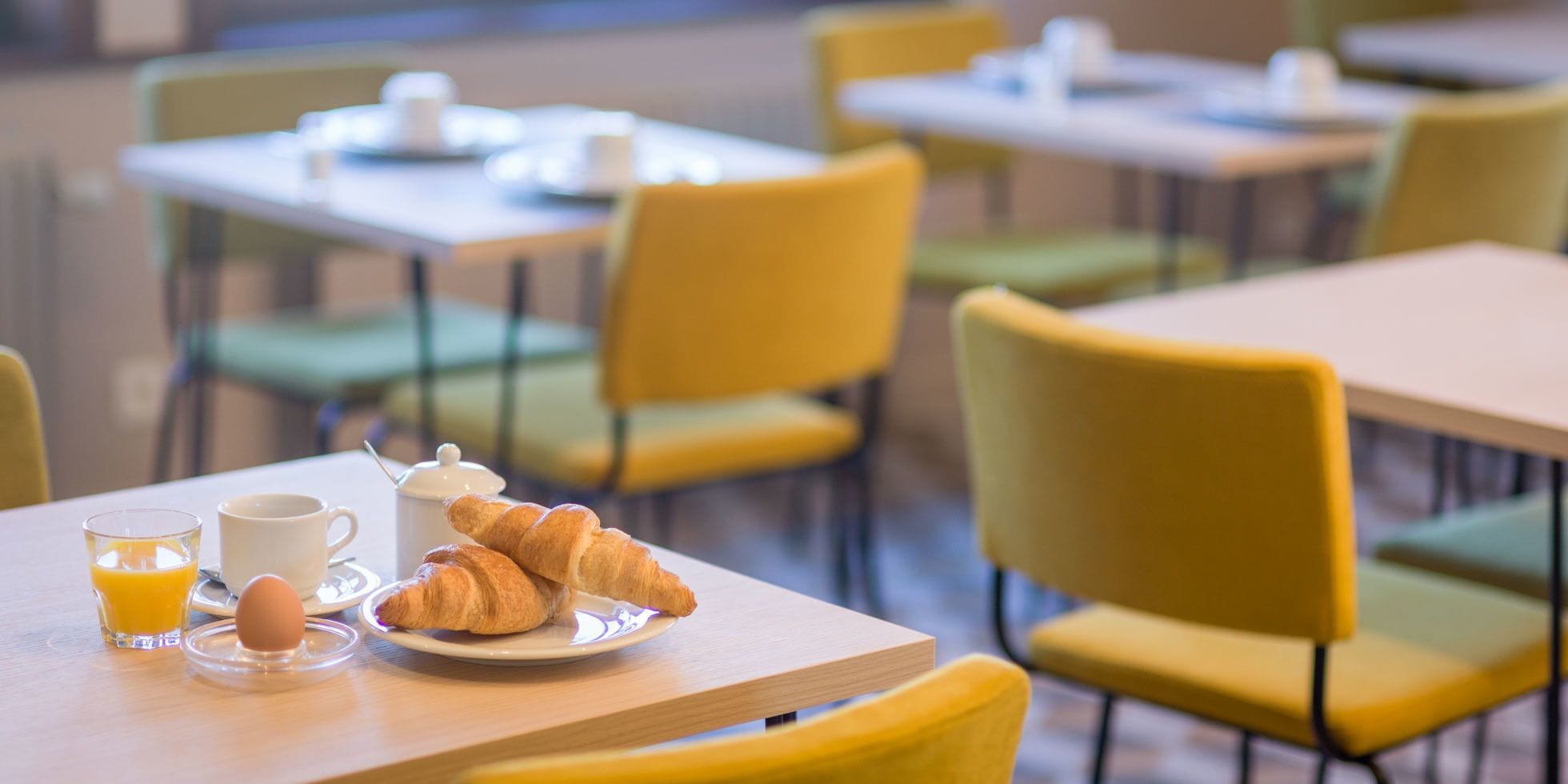 Una mesa de desayuno con croissants, una taza de café y un vaso de jugo de naranja.