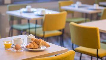 Una mesa de desayuno con croissants, una taza de café y un vaso de jugo de naranja.