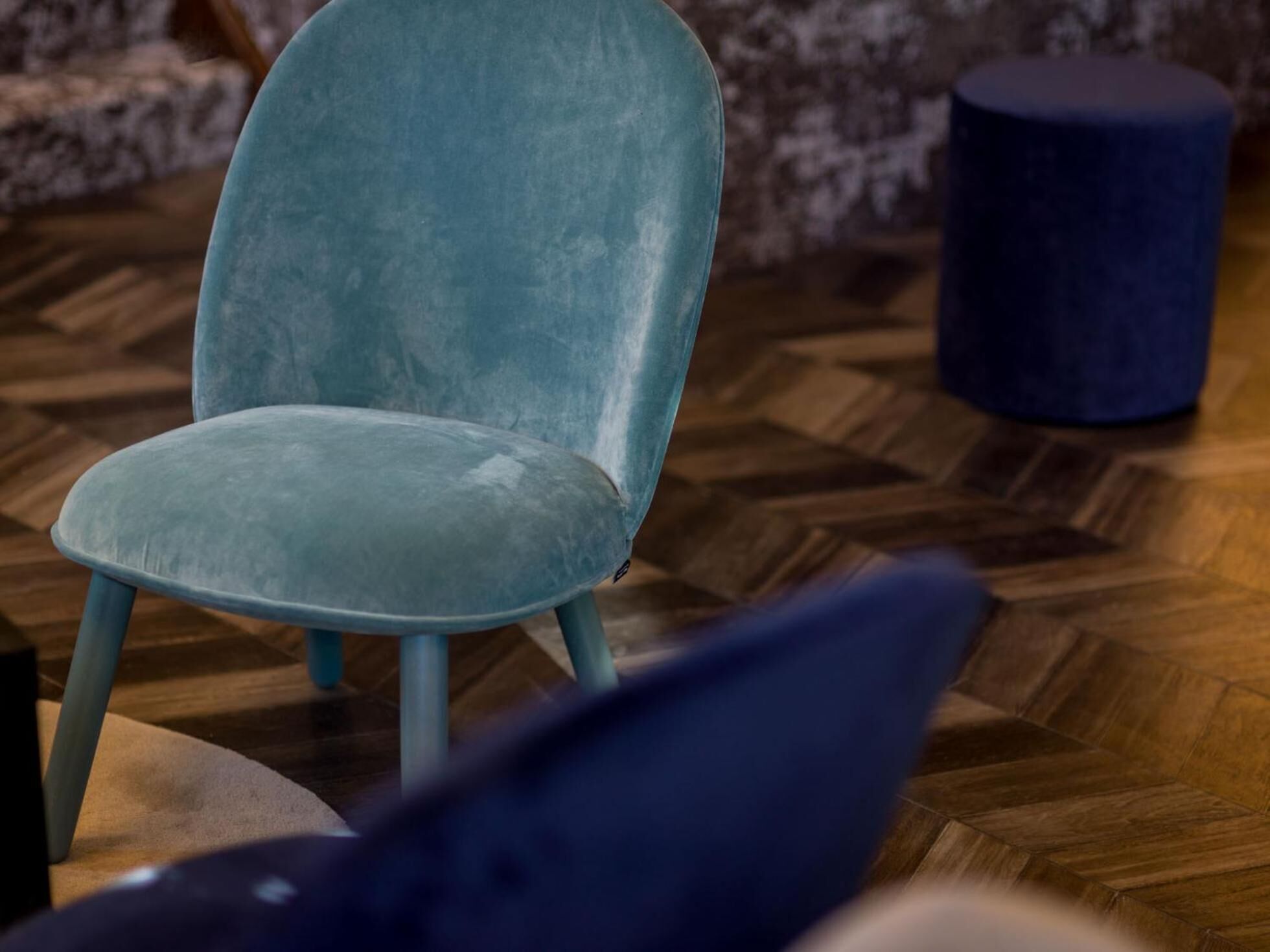 A teal upholstered chair with wooden legs on a herringbone-patterned floor.