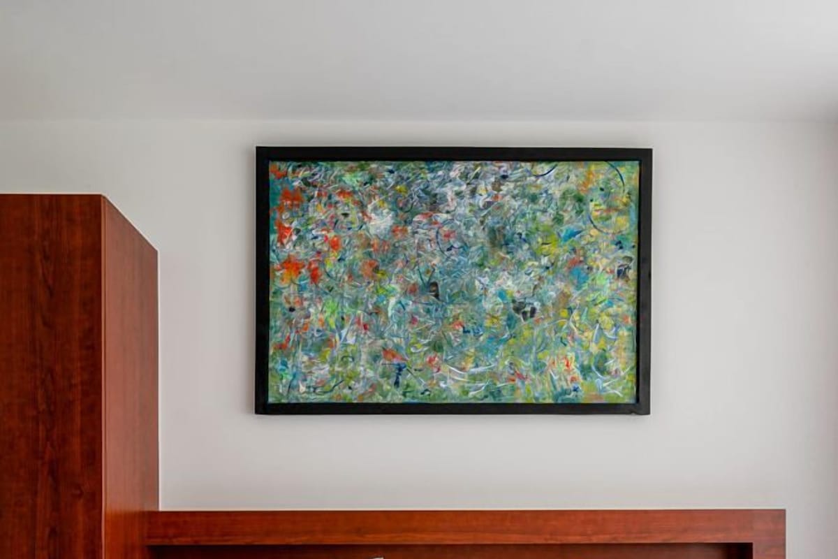A hotel room with a wooden headboard, two pillows, a large abstract painting on the wall, and a bed with white bedding.