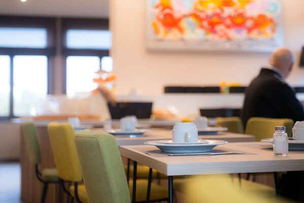 A dining area with tables set for two, chairs, and a decorative centerpiece. - Hotel Olympia (Bruges)