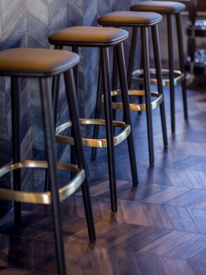 A row of bar stools with metal legs and cushioned seats, arranged against a wall with a herringbone pattern. - Hotel Olympia (Bruges)