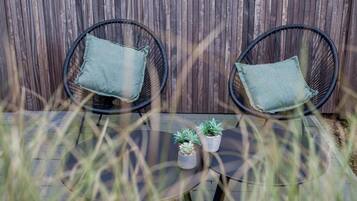 Deux chaises en osier avec des coussins, une petite table ronde et deux plantes en pot.
