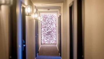 Un couloir d’hôtel avec un mur décoré au fond, des portes de chaque côté et un sol recouvert de moquette.