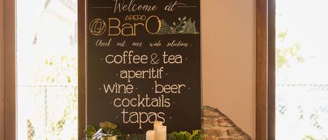 A cozy bar area with a chalkboard sign listing offerings like coffee, tea, aperitifs, wine, beer, cocktails, and tapas.