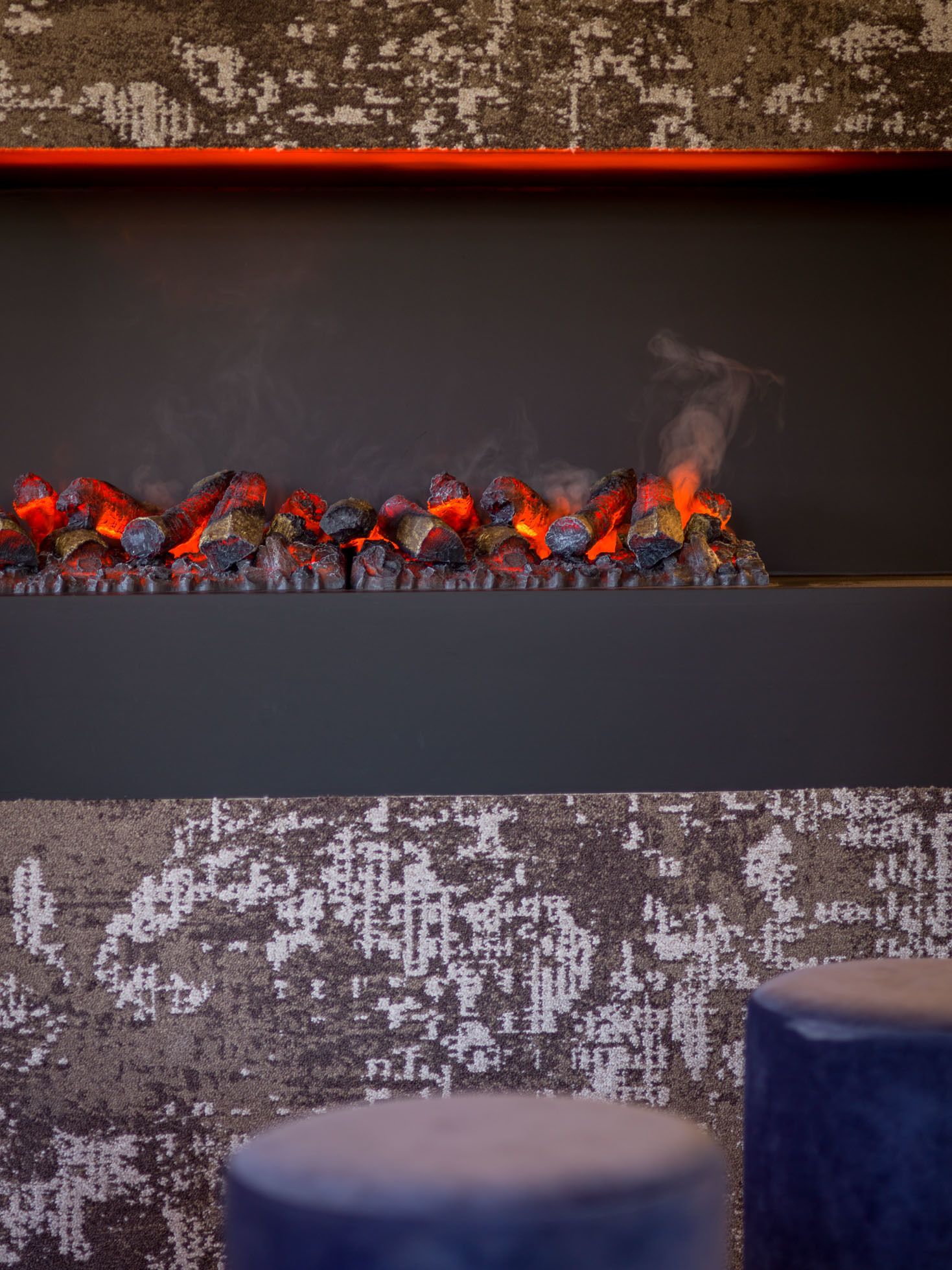 A fireplace with glowing red embers and a patterned wall behind it.