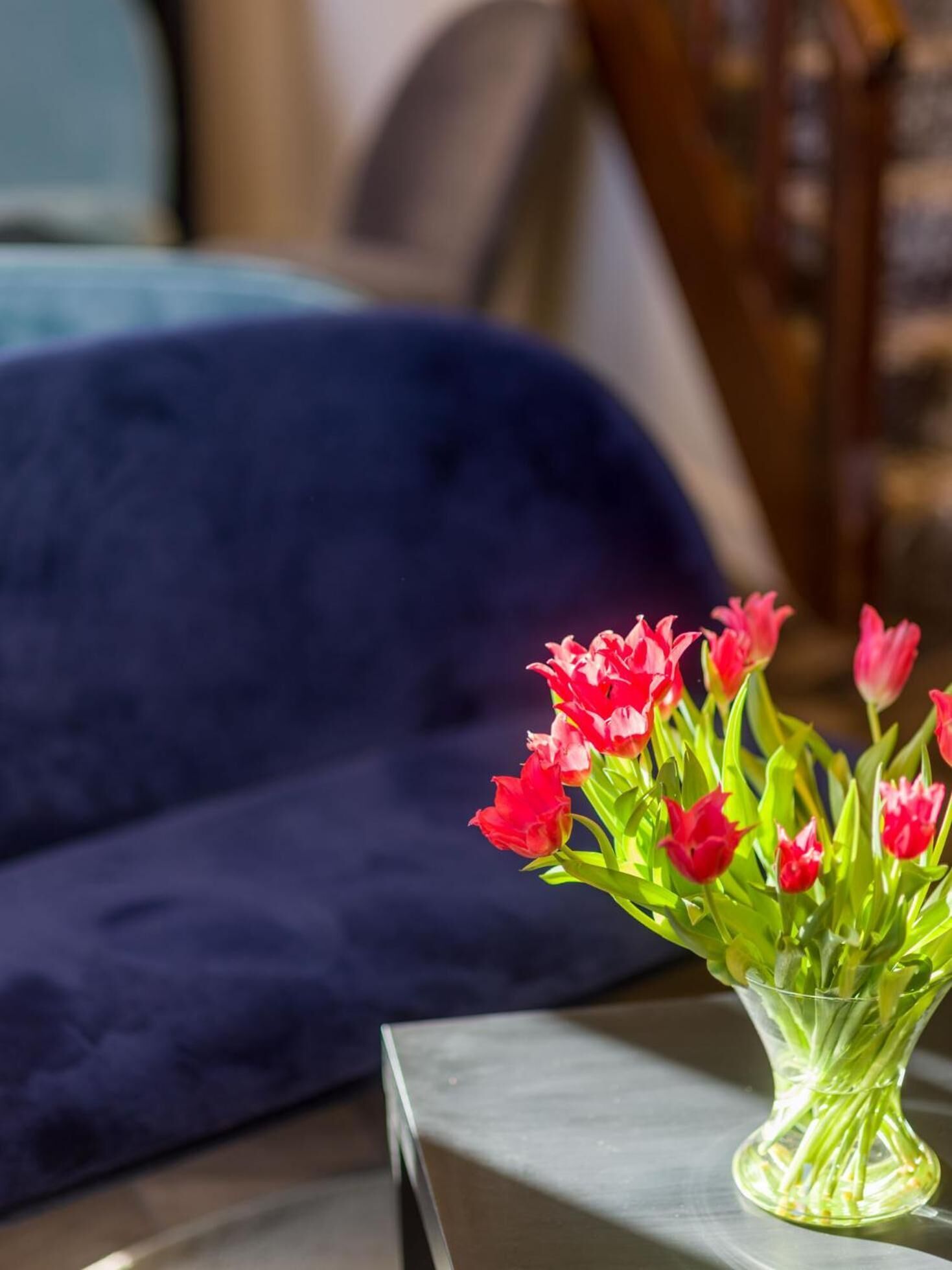 Un jarrón con tulipanes rojos sobre una mesa en una habitación con un sofá azul oscuro.
