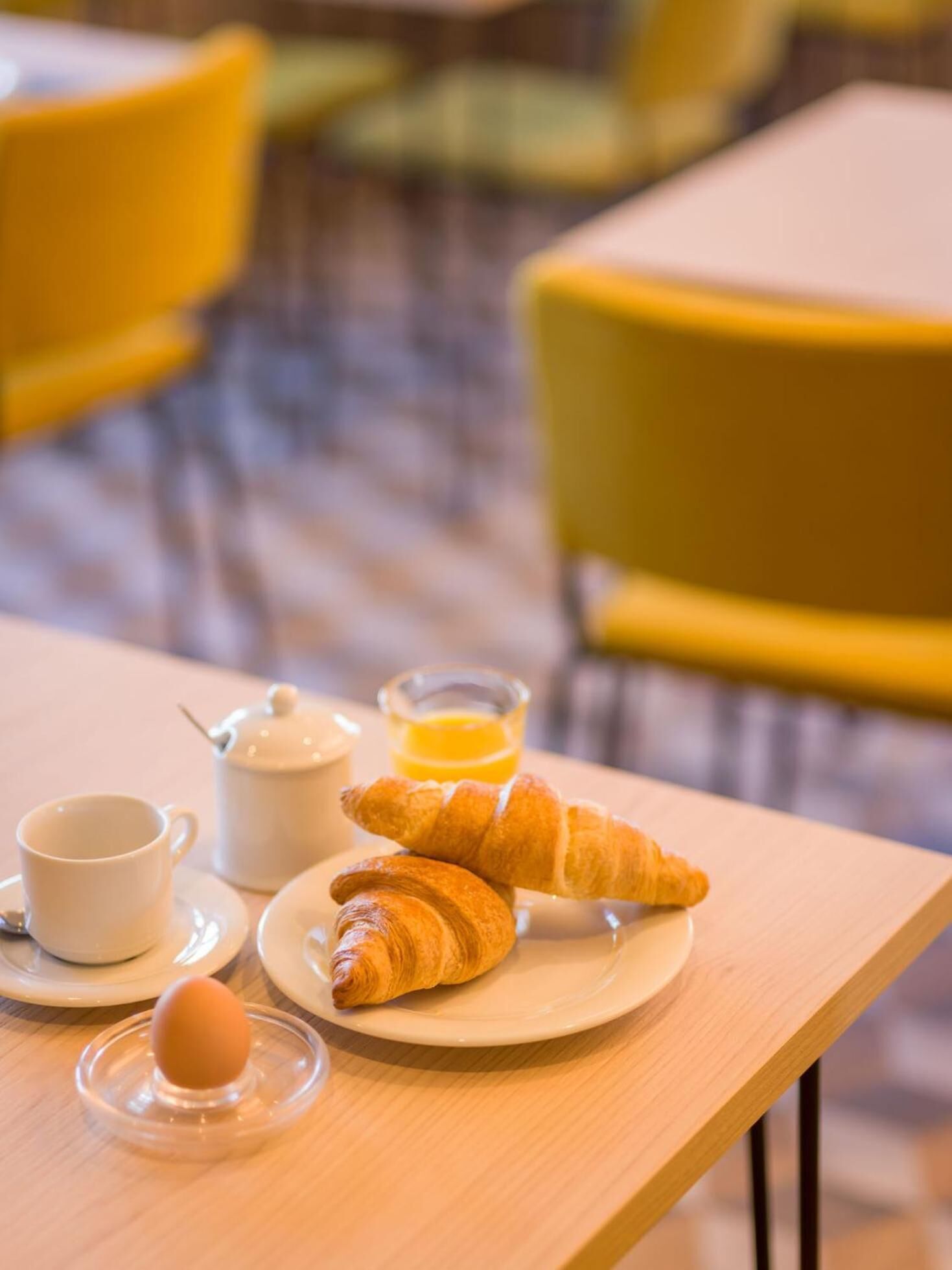Ein Frühstückstisch mit Croissants, einer Kaffeetasse, einem Orangensaftglas und einem Teekessel auf einer Holztischplatte.