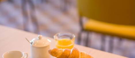 En morgenmadsopsætning med croissanter, en kop kaffe, et glas appelsinjuice og en tepotte på et træbord.