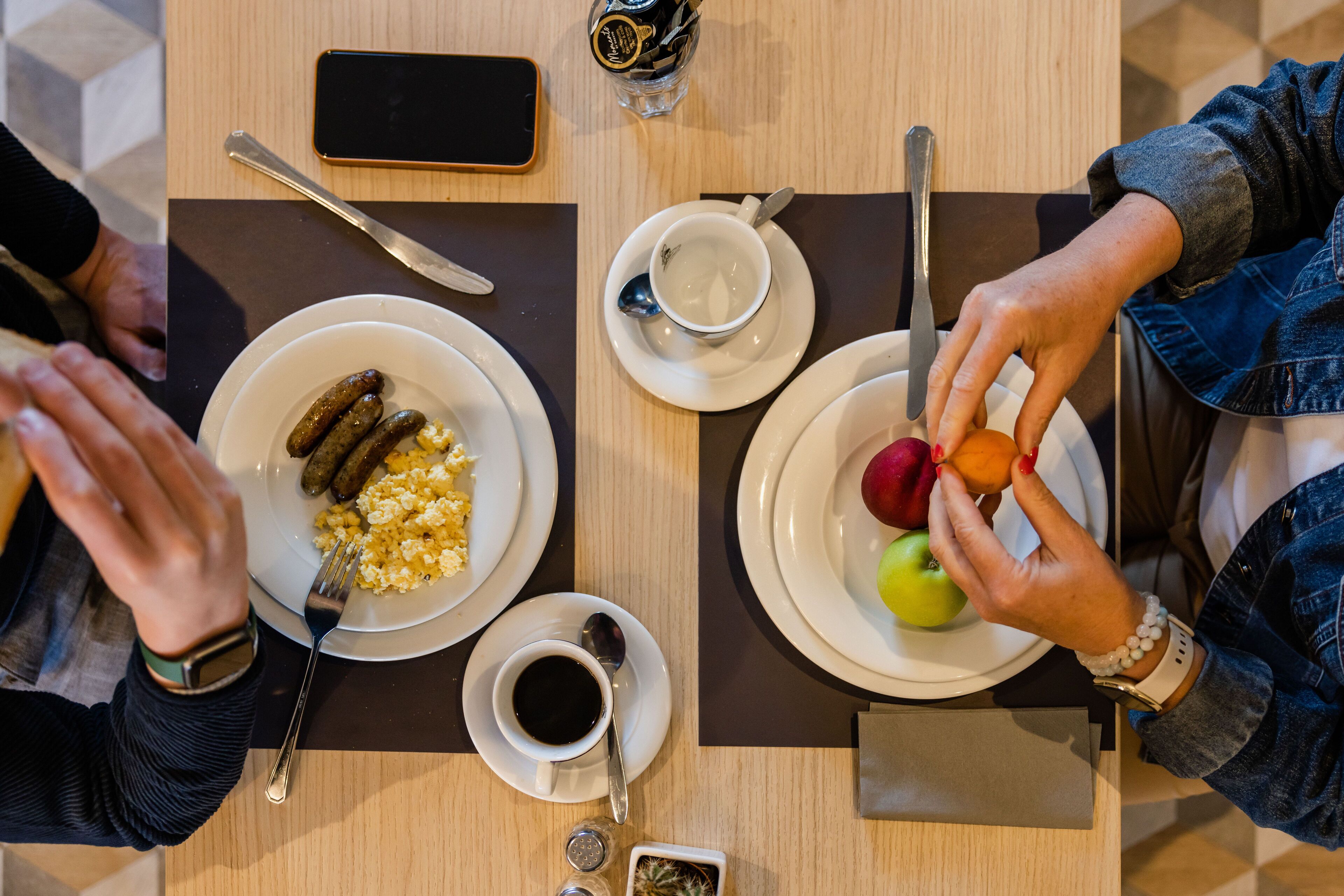 A table with plates of food, a cup of coffee, and a smartphone.