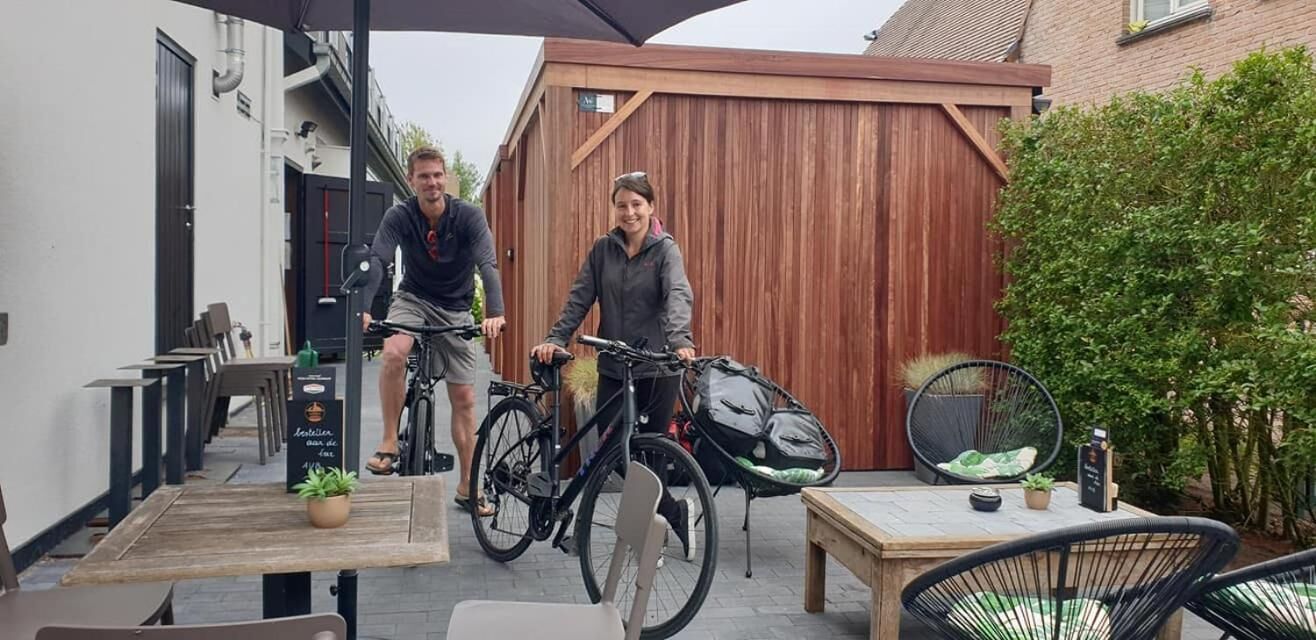An outdoor patio area with wooden tables and chairs, bicycles, and a wooden fence in the background.